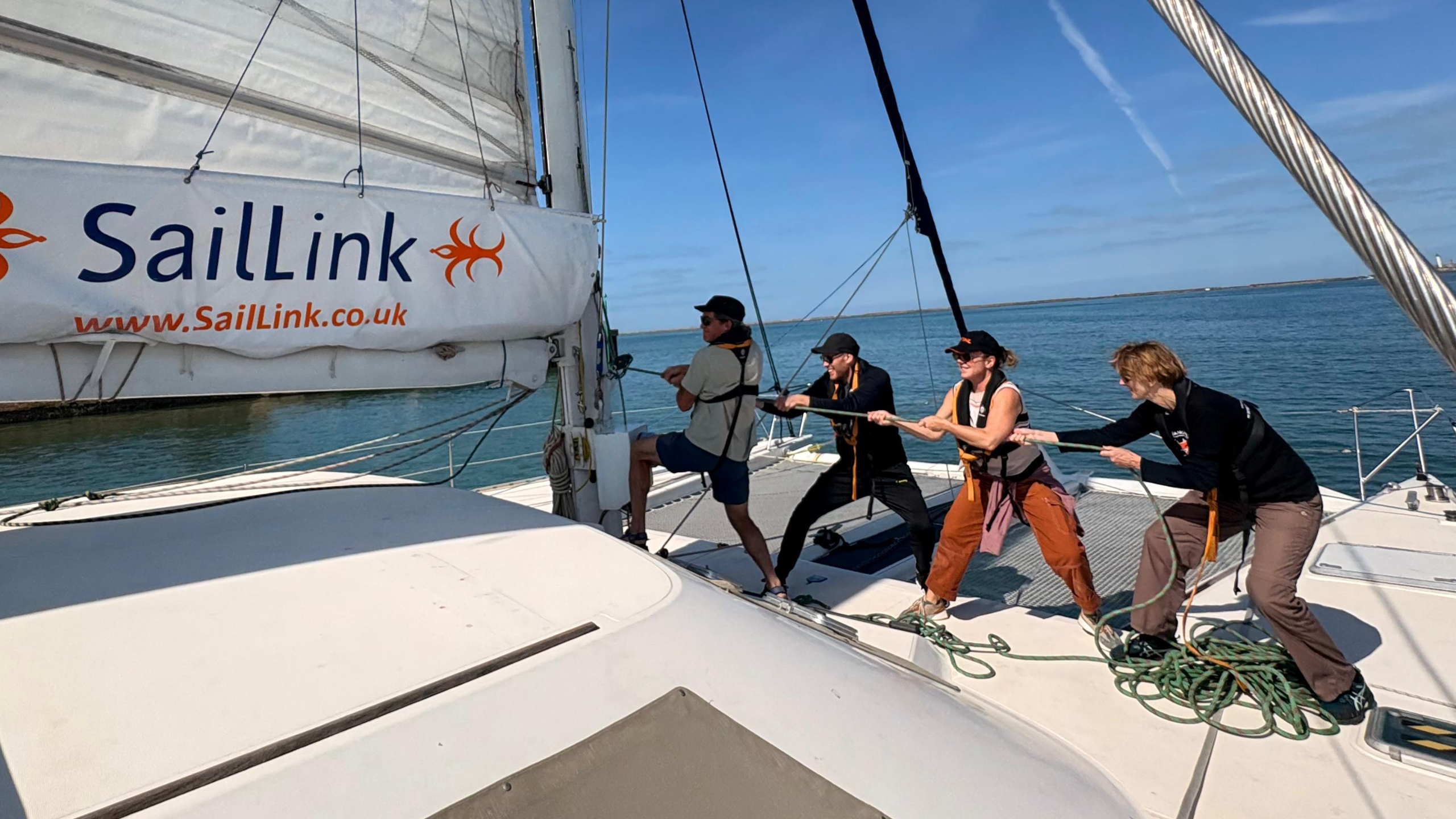Passengers helping to hoist the sail aboard the SailLink catamaran in the Dover Strait